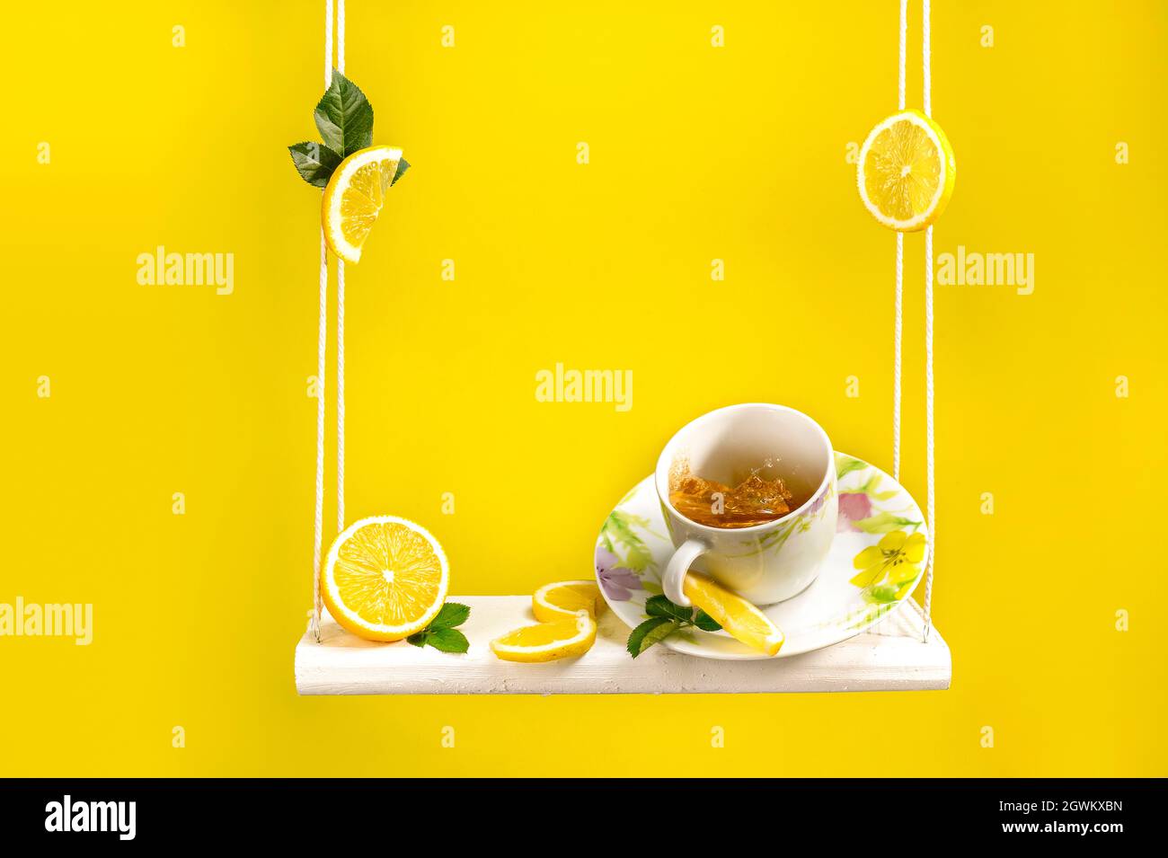 Tasse de thé assis sur une balançoire avec beaucoup de citron frais coupé autour et beau fond jaune vif Banque D'Images