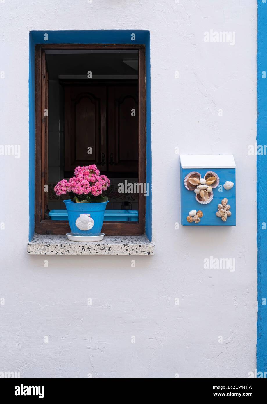 fenêtre bleue sur une façade blanche d'une maison dans un village de pêcheurs, avec un pot de fleurs violettes et une boîte aux lettres bleue avec ornements de seashell, verticale Banque D'Images