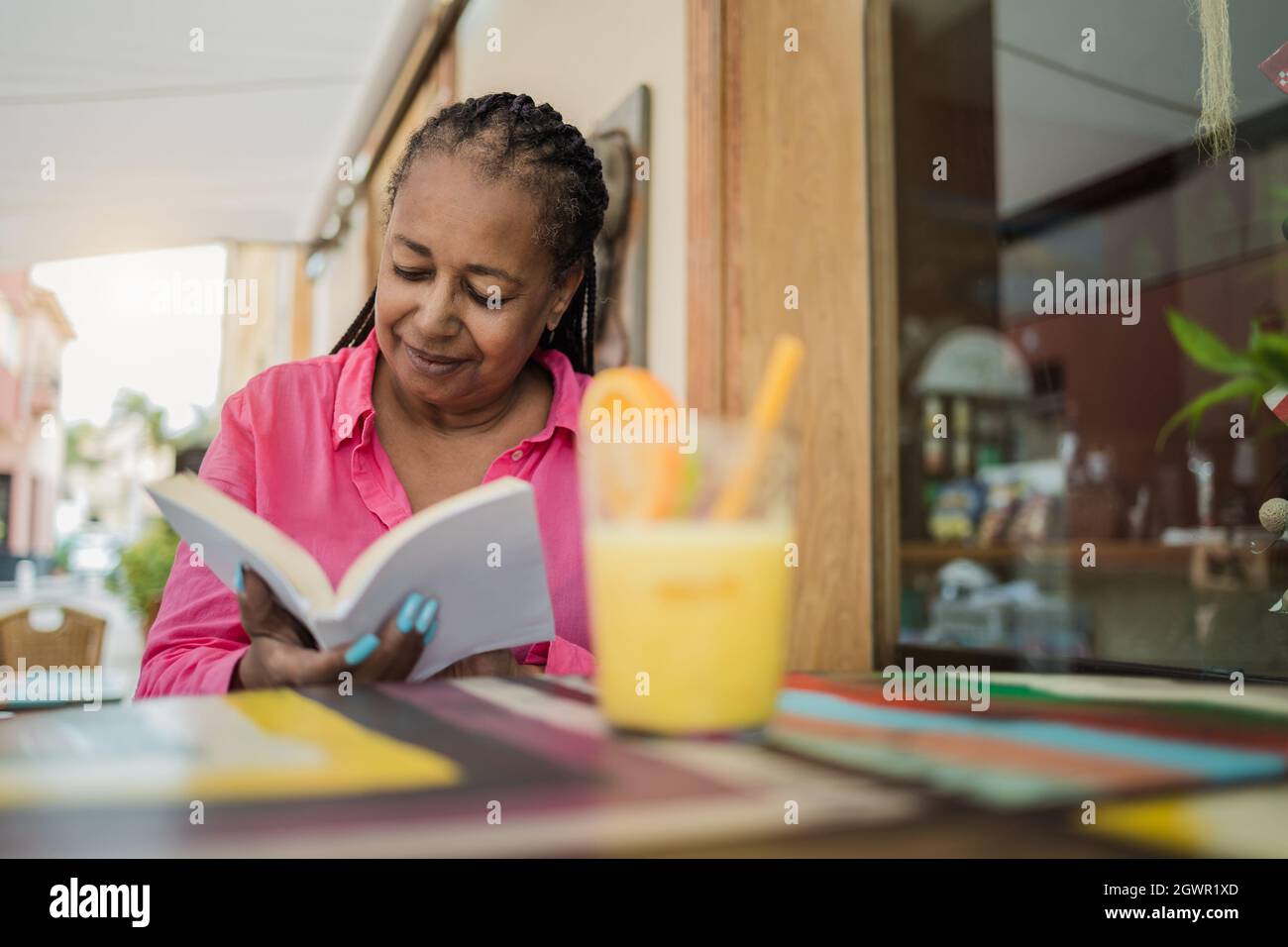 Femme africaine senior s'amusant à lire un livre pendant le brunch en plein air au bar-restaurant - Focus on face Banque D'Images