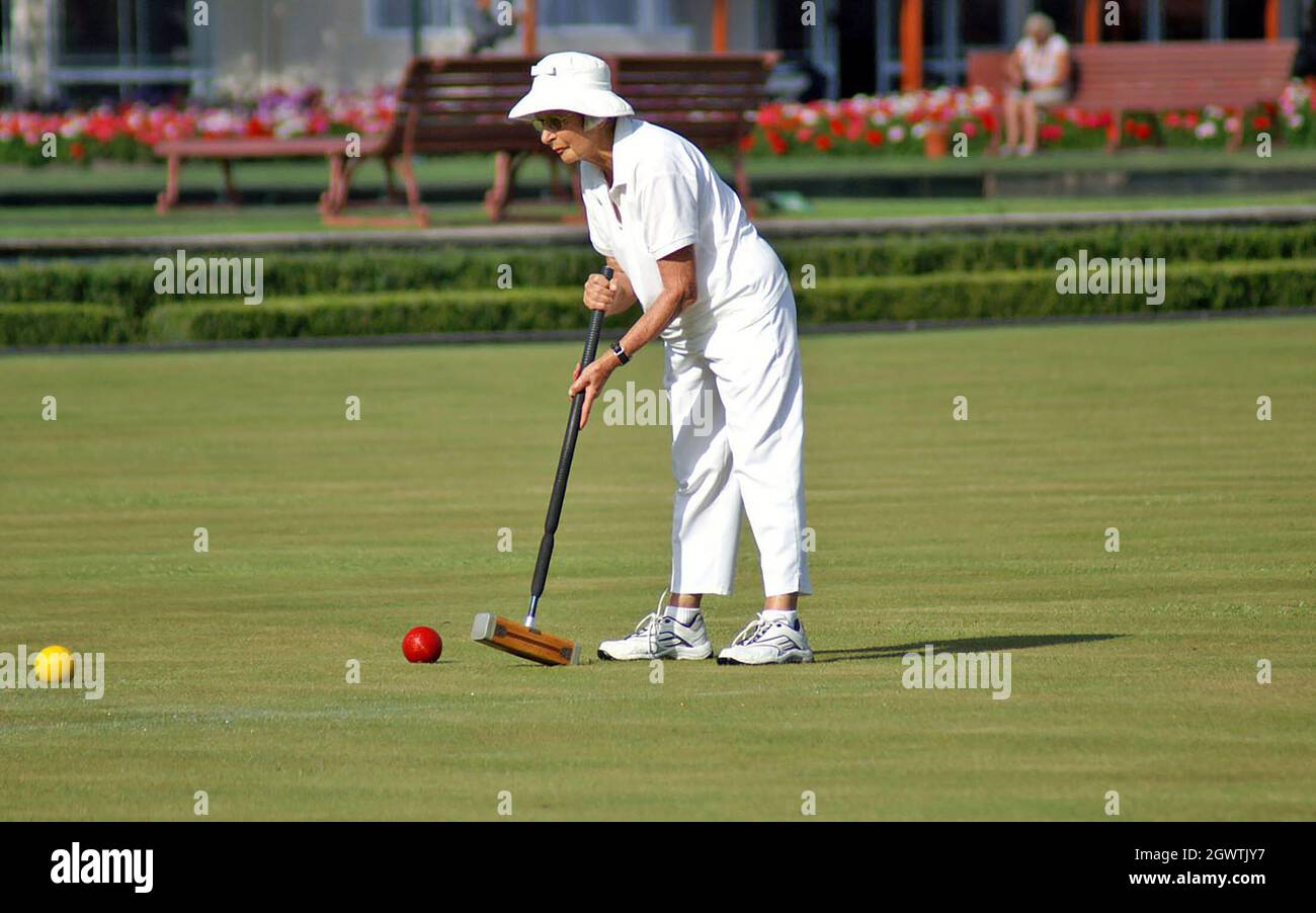 Une femme plus âgée en blanc joue du croquet à l'aide d'un maillet traditionnel pour frapper une balle rouge à Rotorua, en Nouvelle-Zélande. Banque D'Images