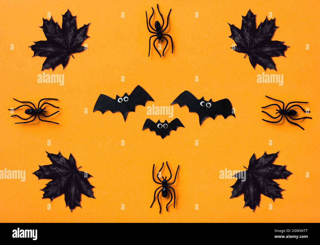 Décorations d'Halloween sur fond orange, plat. Vue de dessus des chauves-souris, des araignées noires et des feuilles d'érable. Motif sinistre avec des objets pour Hallowen celeb Banque D'Images