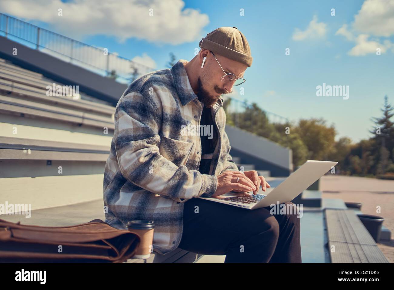 Homme barbu concentré assis à l'extérieur et en tapant du texte sur un ordinateur portable. Connexion Internet 4G Banque D'Images