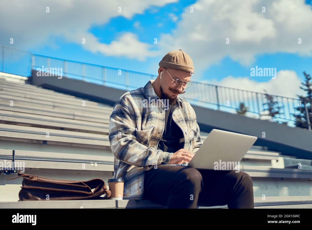 Homme barbu concentré assis à l'extérieur et en tapant du texte sur un ordinateur portable. Connexion Internet 4G Banque D'Images
