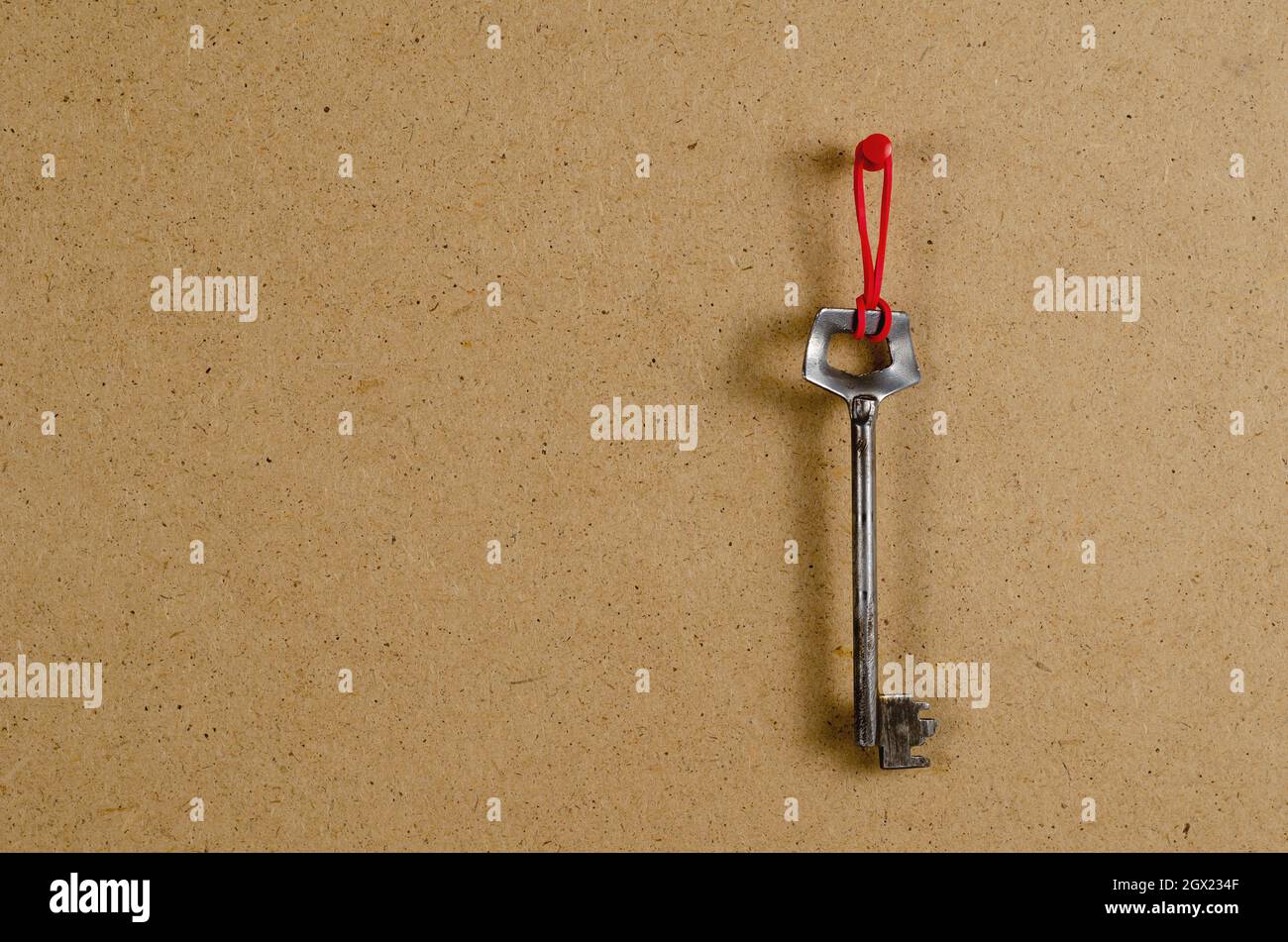 Une grande clé de porte en métal en face du fond marron. L'ancienne clé est suspendue verticalement sur une bande en caoutchouc rouge. Vue latérale. Copier l'espace Banque D'Images