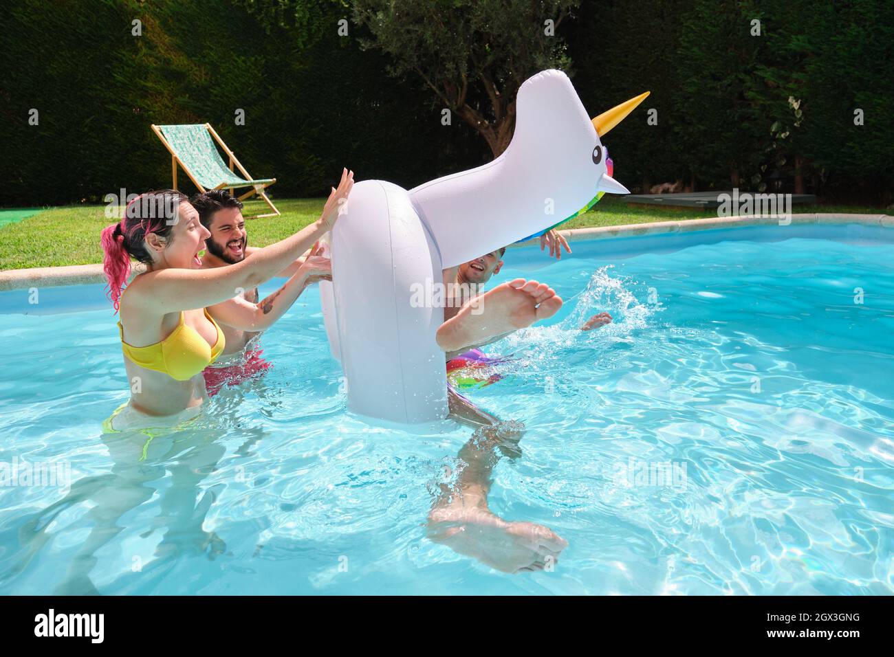 Deux amis qui jettent un homme d'une licorne arc-en-ciel flottent dans la piscine. Banque D'Images