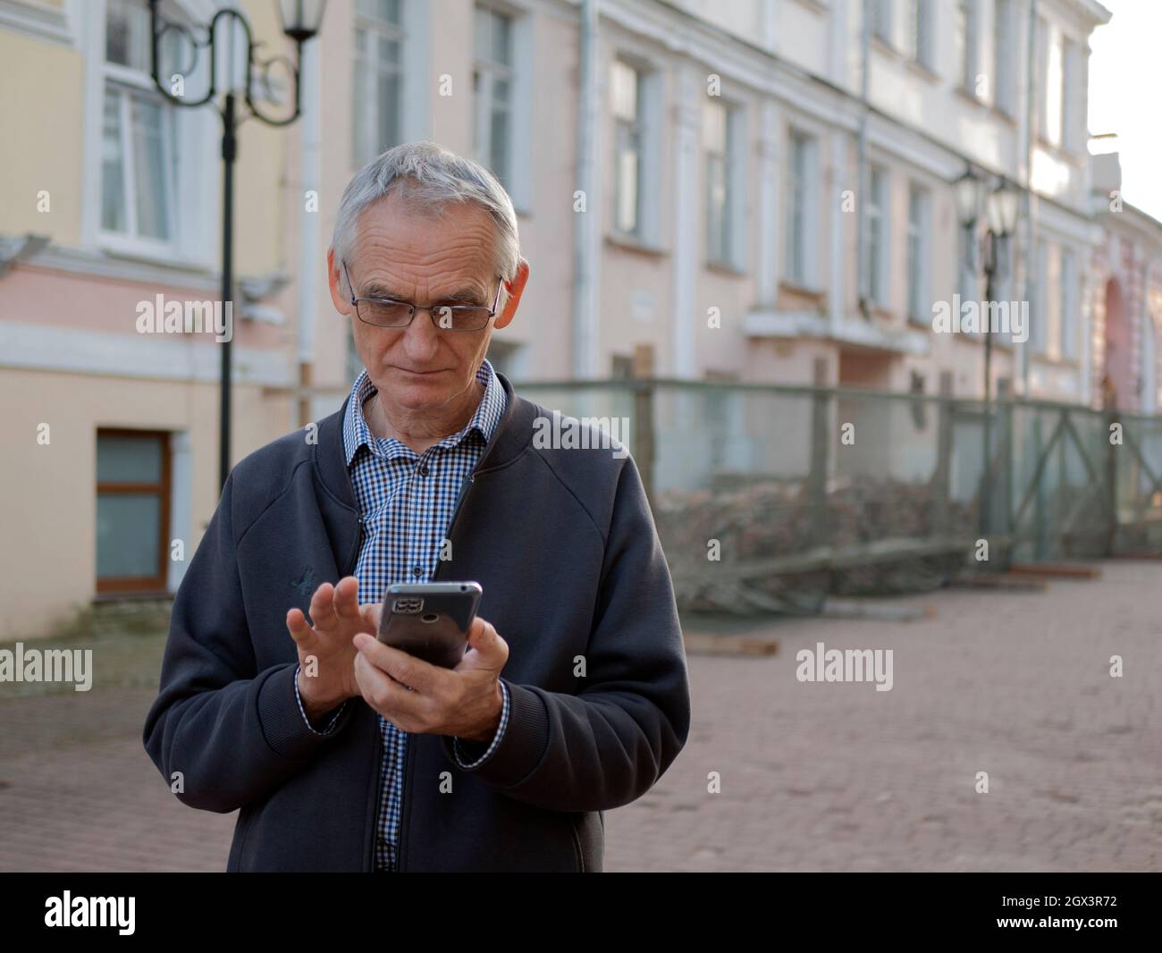 Une personne âgée dans les lunettes tient un téléphone portable dans ses mains. Un homme âgé envoie des SMS sur un smartphone. Le vieil homme utilise un téléphone portable Banque D'Images