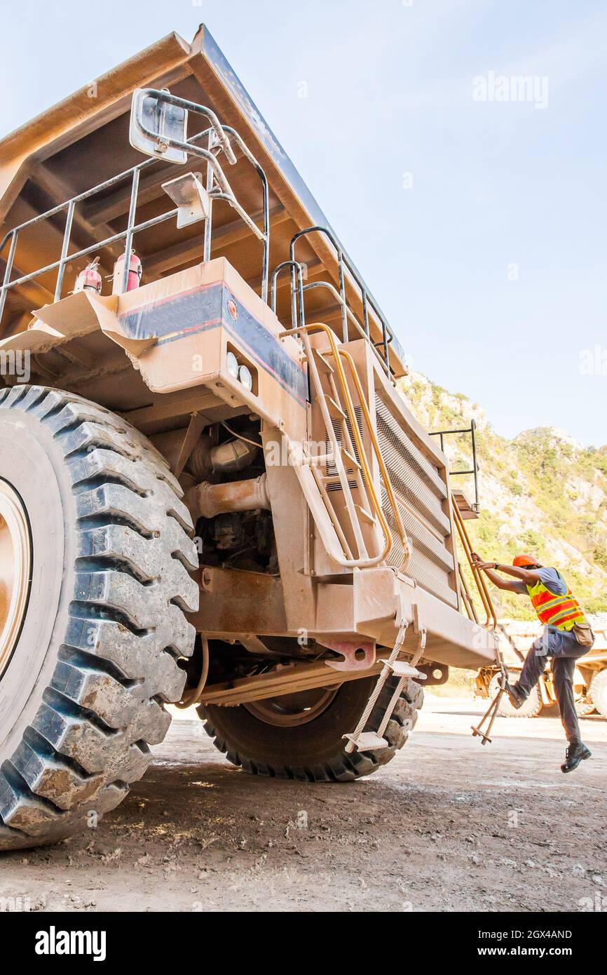 Un chauffeur de sexe masculin se promène dans les escaliers d'un grand camion de benne de carrière dans un espace ouvert.Transport. Banque D'Images