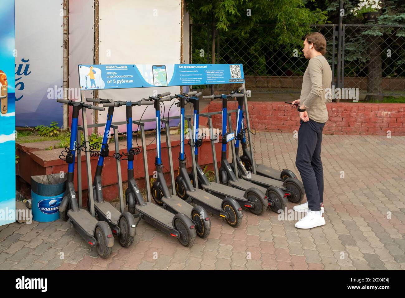 Un gars se tient à un comptoir avec des scooters électriques pour le mouvement mobile autour de la ville et lit les règles de location écrites en russe. Banque D'Images