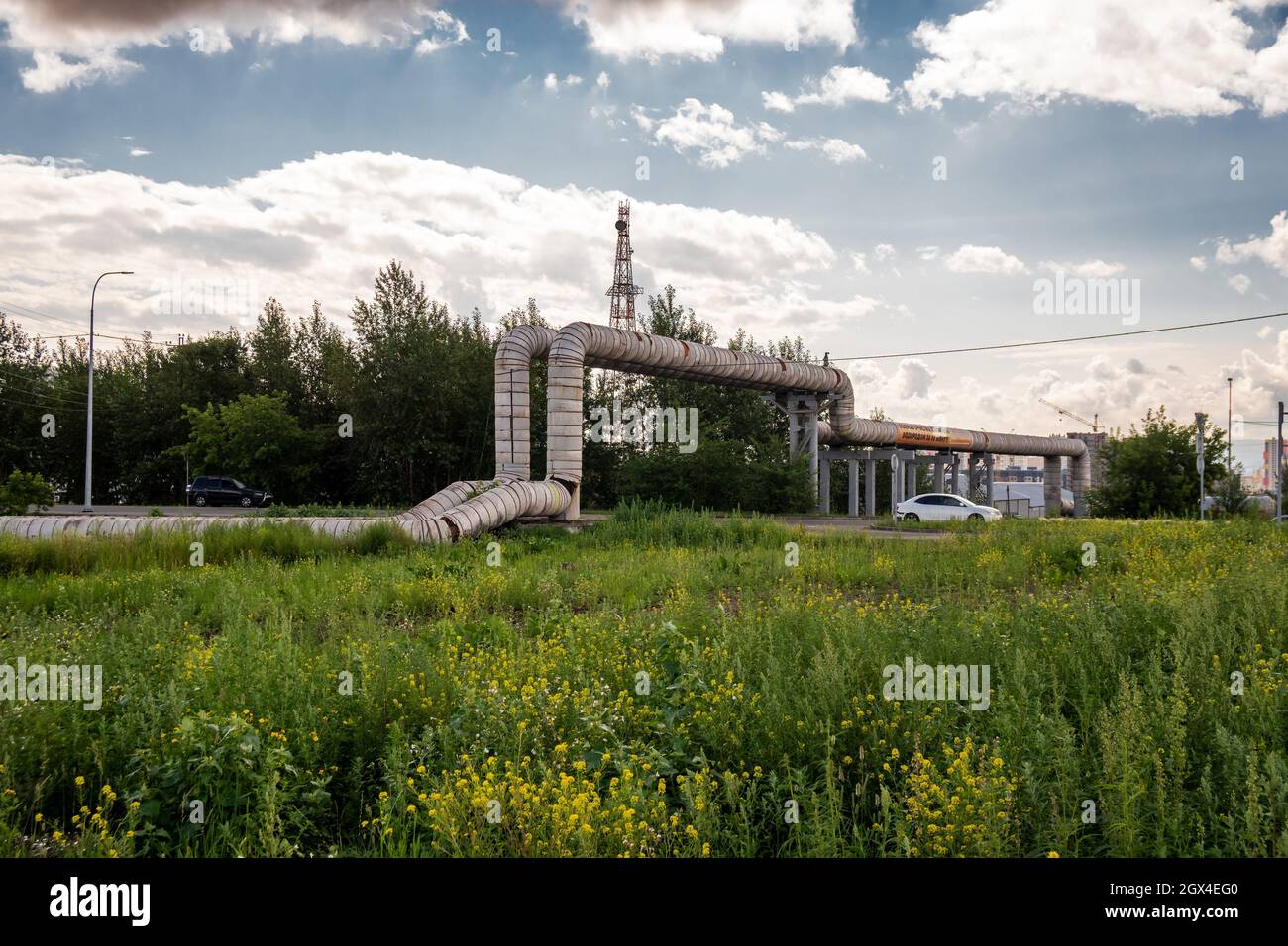 Le pipeline côtier de la principale centrale de chauffage de la ville du réseau de chauffage principal passe sur la route avec des voitures de conduite pendant une journée d'été. Banque D'Images