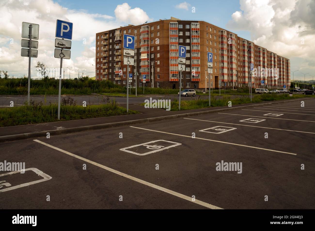 Places de stationnement pour personnes handicapées avec panneaux de signalisation routière, délimitées sur l'asphalte, en arrière-plan d'un bâtiment résidentiel. Banque D'Images