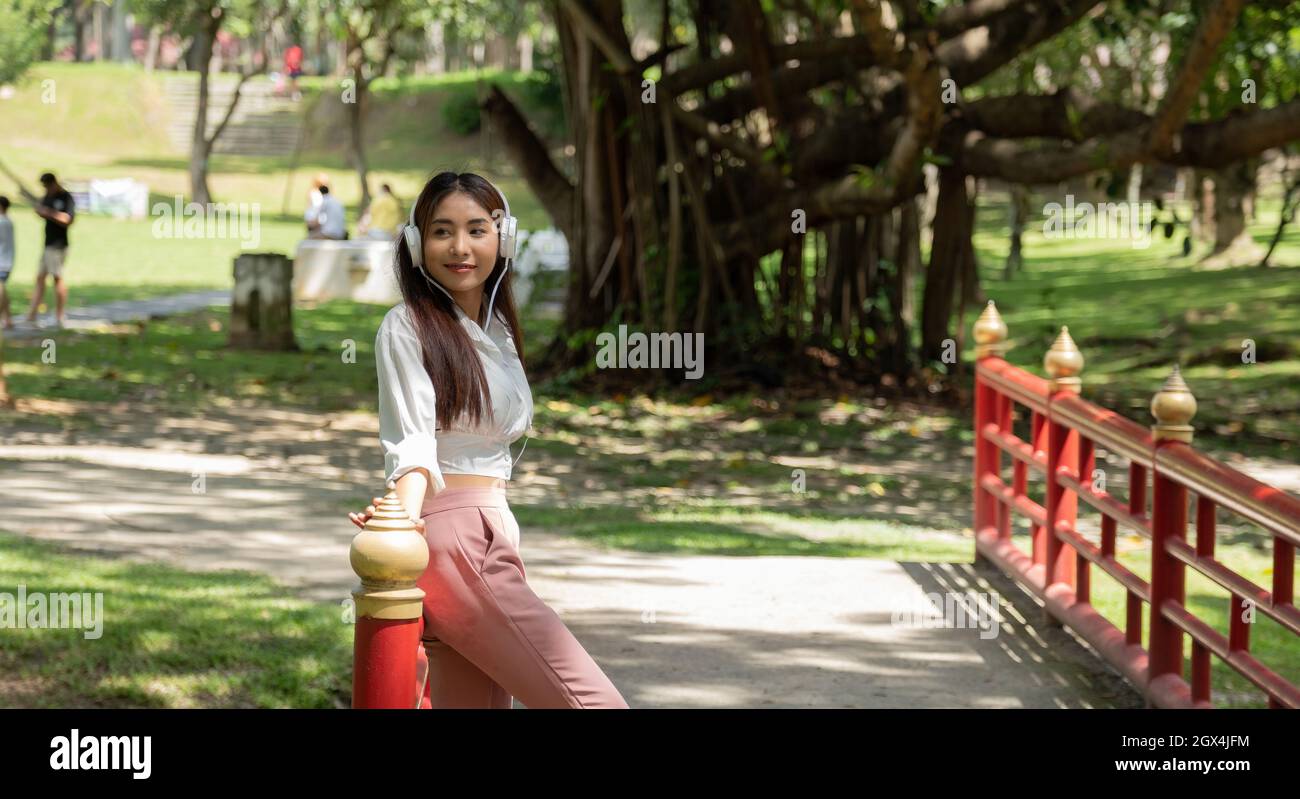 Portrait Asian Student Girl Wearing Headphones, debout sur la pelouse dans le parc Banque D'Images