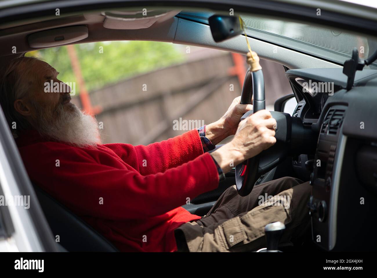 Ancien retraité senior homme avec une longue barbe conduisant une voiture grise Banque D'Images