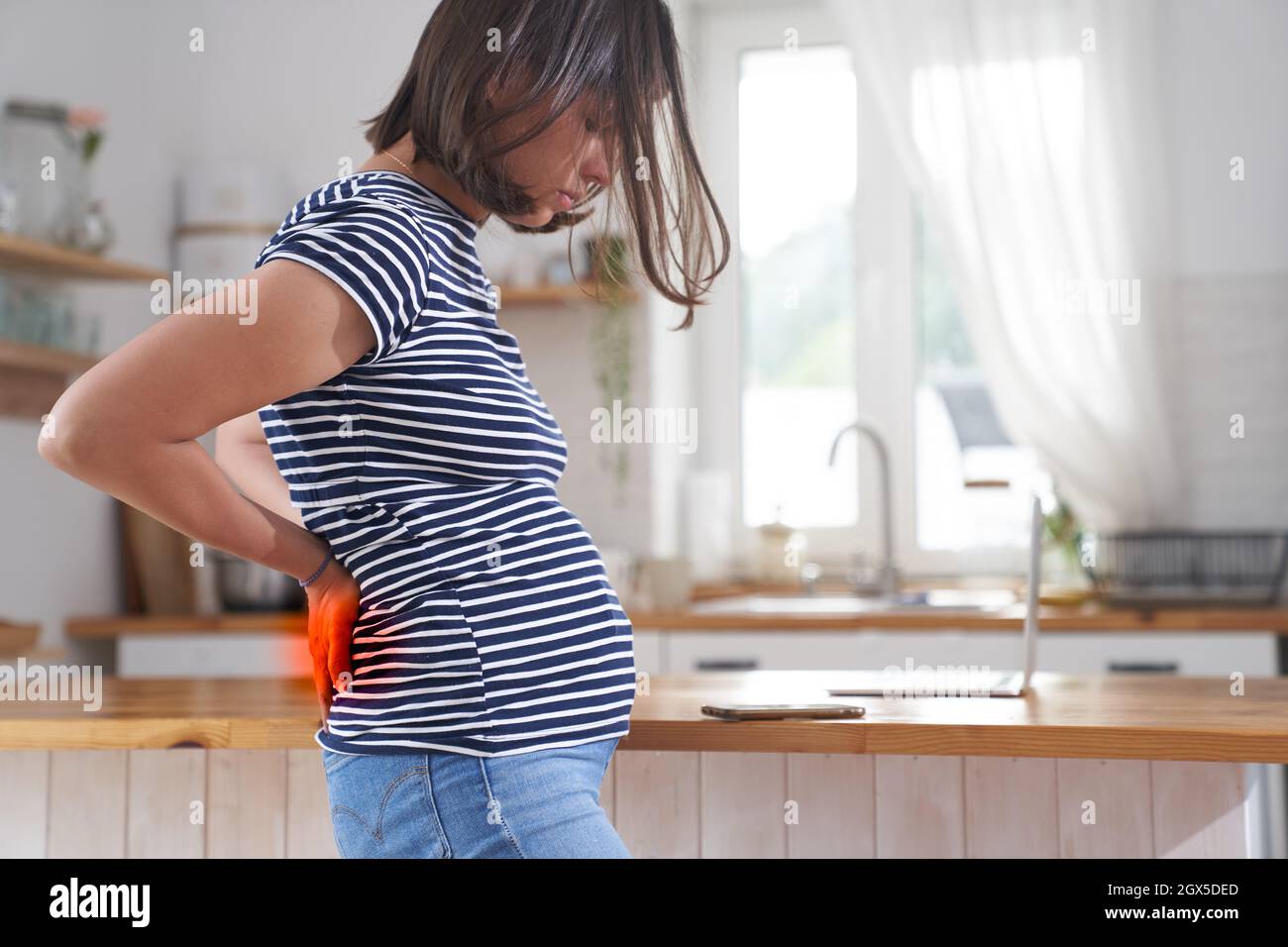 Une jeune femme enceinte la tient avec les mains. Un brunette dans le troisième trimestre de la grossesse. Le concept de douleur dorsale pendant la grossesse. Photo de haute qualité Banque D'Images