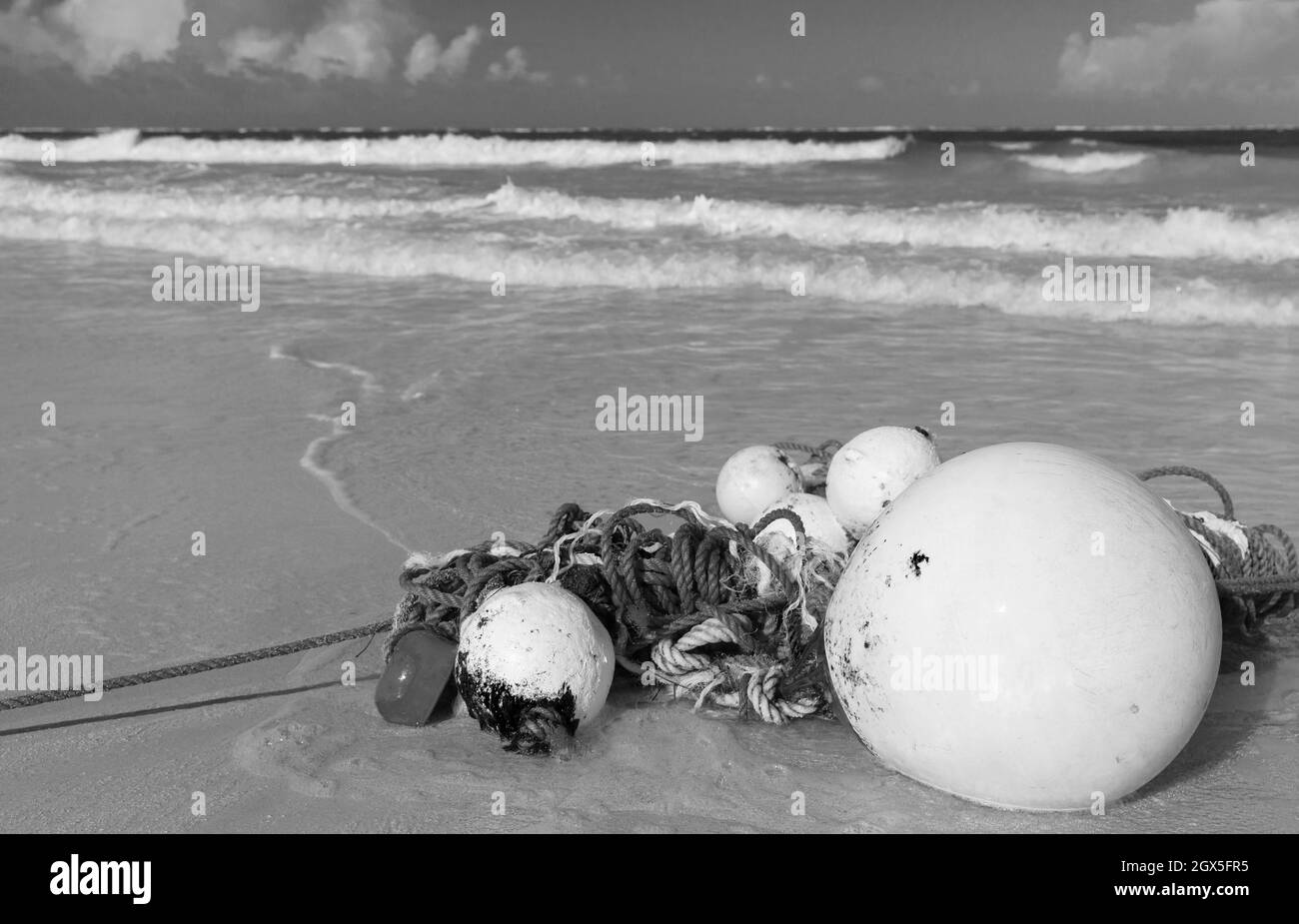 Des flotteurs et une corde reposent sur une côte de sable humide. Photo stylisée vintage en noir et blanc Banque D'Images