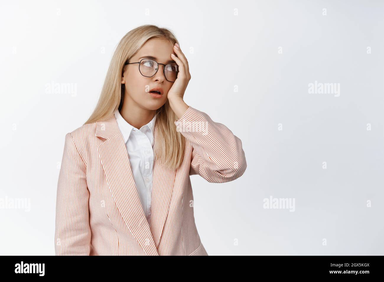 Jeune employée de bureau agacée, yeux roulés et visage fatigués, irrités avec quelque chose, debout dans le costume et les lunettes sur fond blanc Banque D'Images