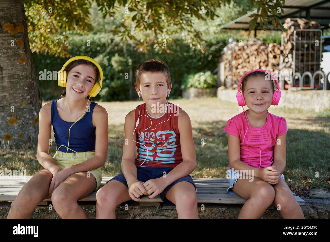 Trois enfants sourient devant la caméra pendant qu'ils sont assis au-dessus de la pierre et écoutent de la musique. Trois enfants utilisent leur casque et leurs écouteurs pour lis Banque D'Images