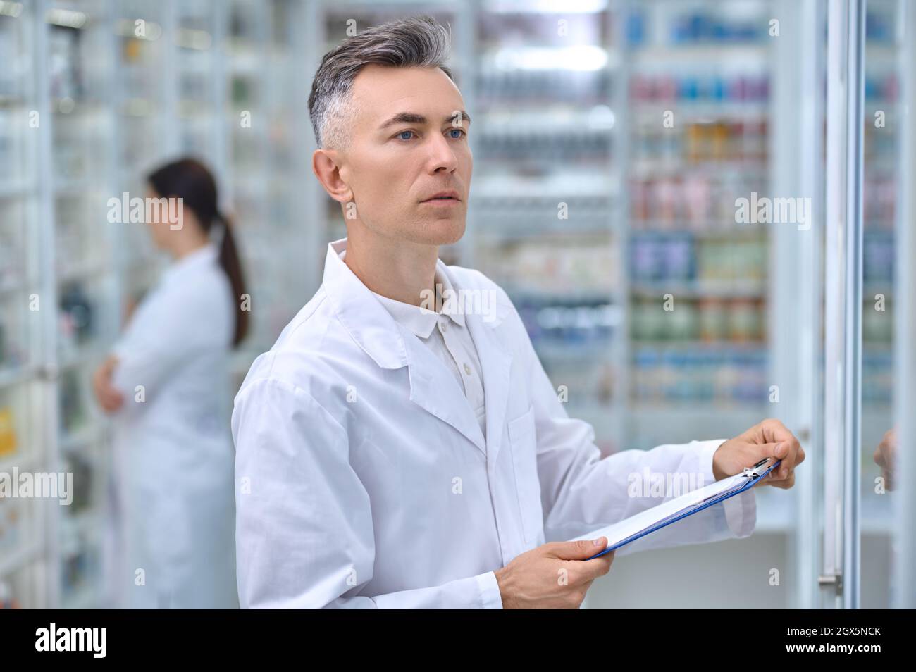 Homme avec dossier regardant des étagères avec des médicaments Banque D'Images