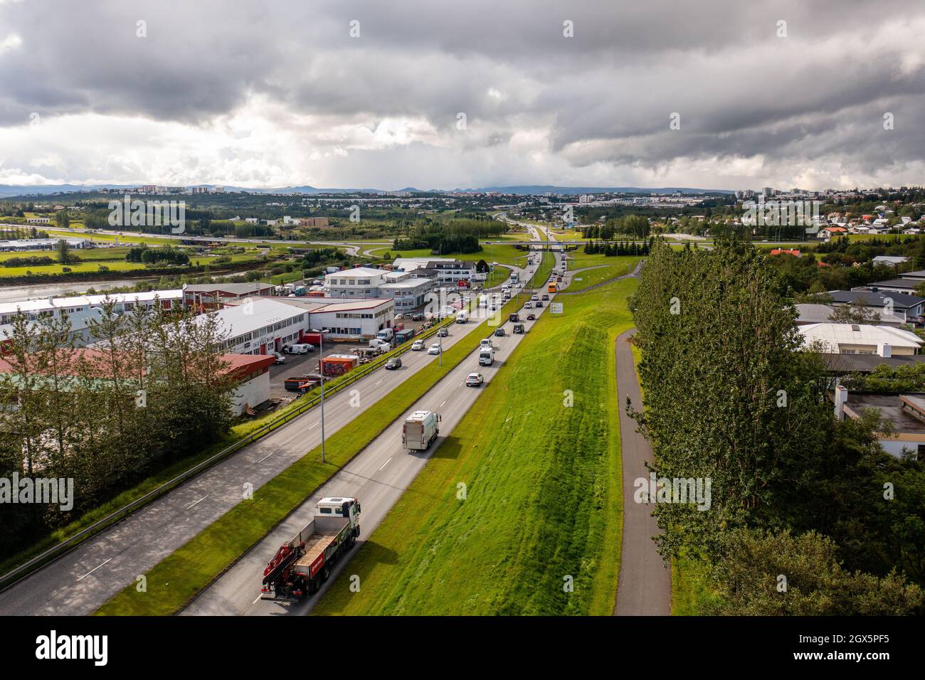 Vue de drone des camions et des voitures roulant sur la route asphaltée près des arbres verts et des bâtiments à travers la ville le jour d'été couvert. Banque D'Images
