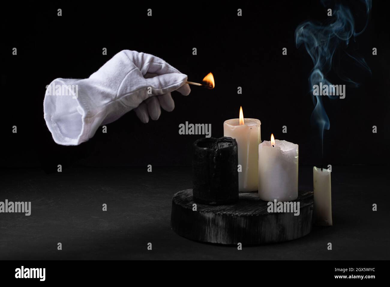 Main invisible dans un gant blanc éclairant des bougies avec un match, fumée  de bougie sur un fond noir, effrayant halloween concept, gros plan Photo  Stock - Alamy