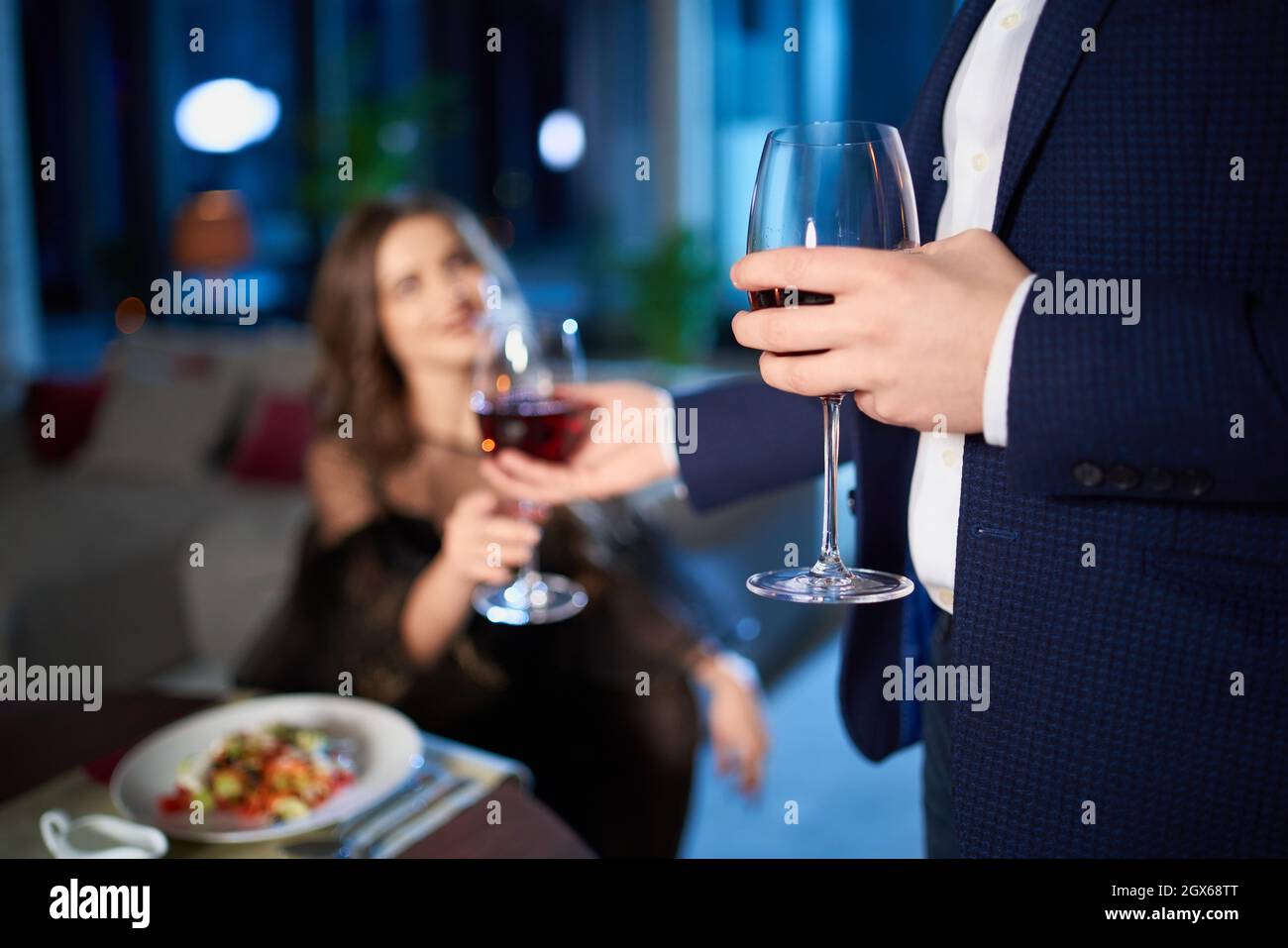 Beau jeune couple en tenue élégante passer le soir à la maison pour un dîner romantique.Homme donnant un verre de vin rouge à une charmante femme.Gros plan. Banque D'Images