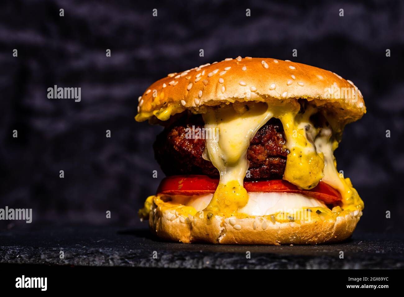 Gros plan d'un savoureux hamburger de bœuf frais avec fromage fondu sur fond noir Banque D'Images