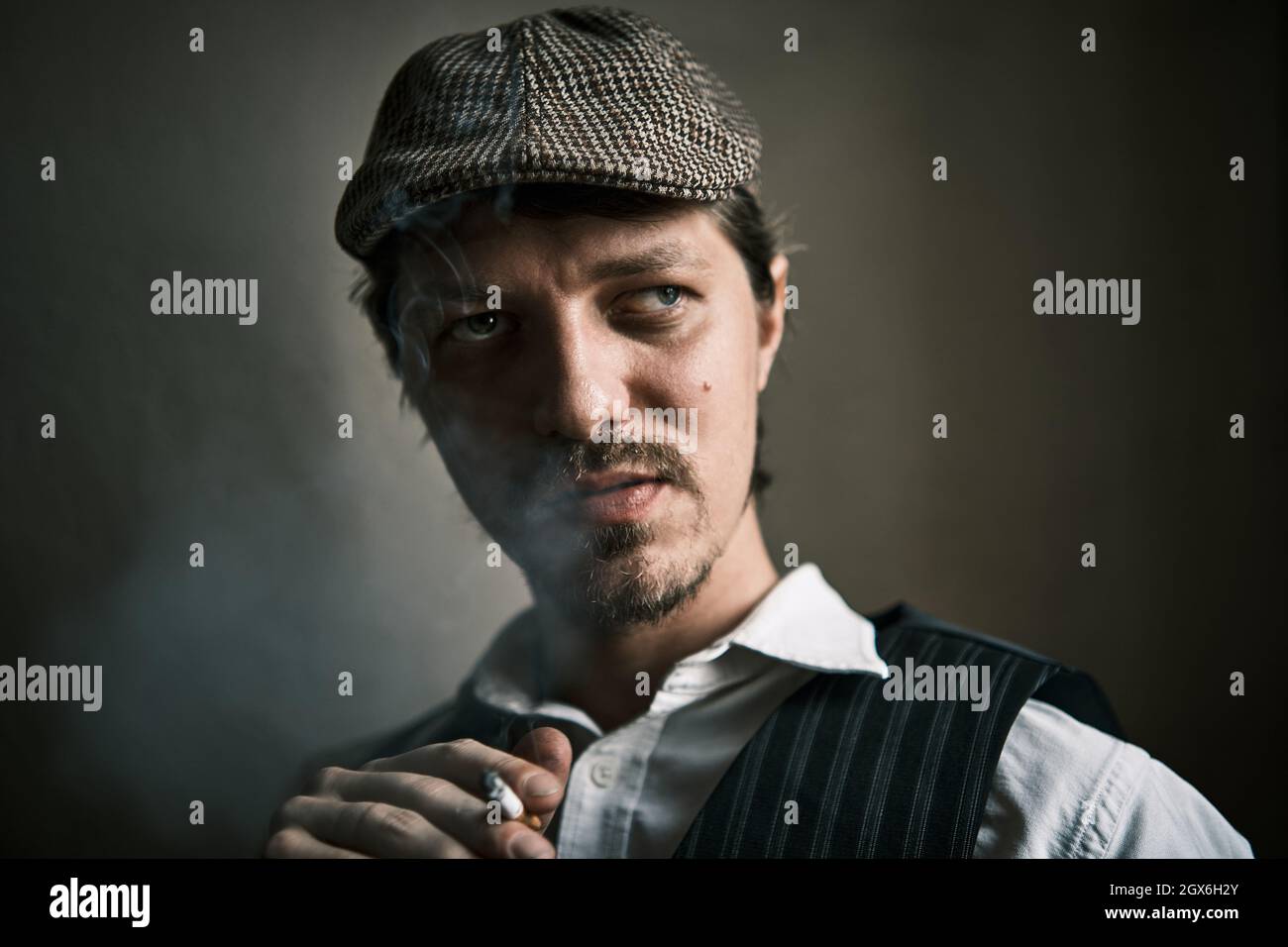 Un jeune homme fume une cigarette, souffle de la fumée, habillé dans un style rétro, dans un béret, une prise de vue cinématographique, gros plan Banque D'Images