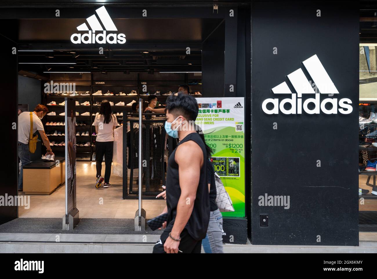 Des piétons marchent devant la marque allemande multinationale de vêtements de sport Adidas magasin et logo à Hong Kong. Banque D'Images