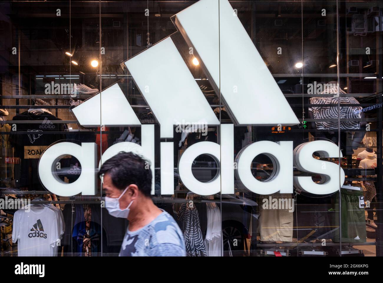Un homme portant un masque passe devant la marque allemande de vêtements de sport multinationaux Adidas Store et le logo à Hong Kong. Banque D'Images