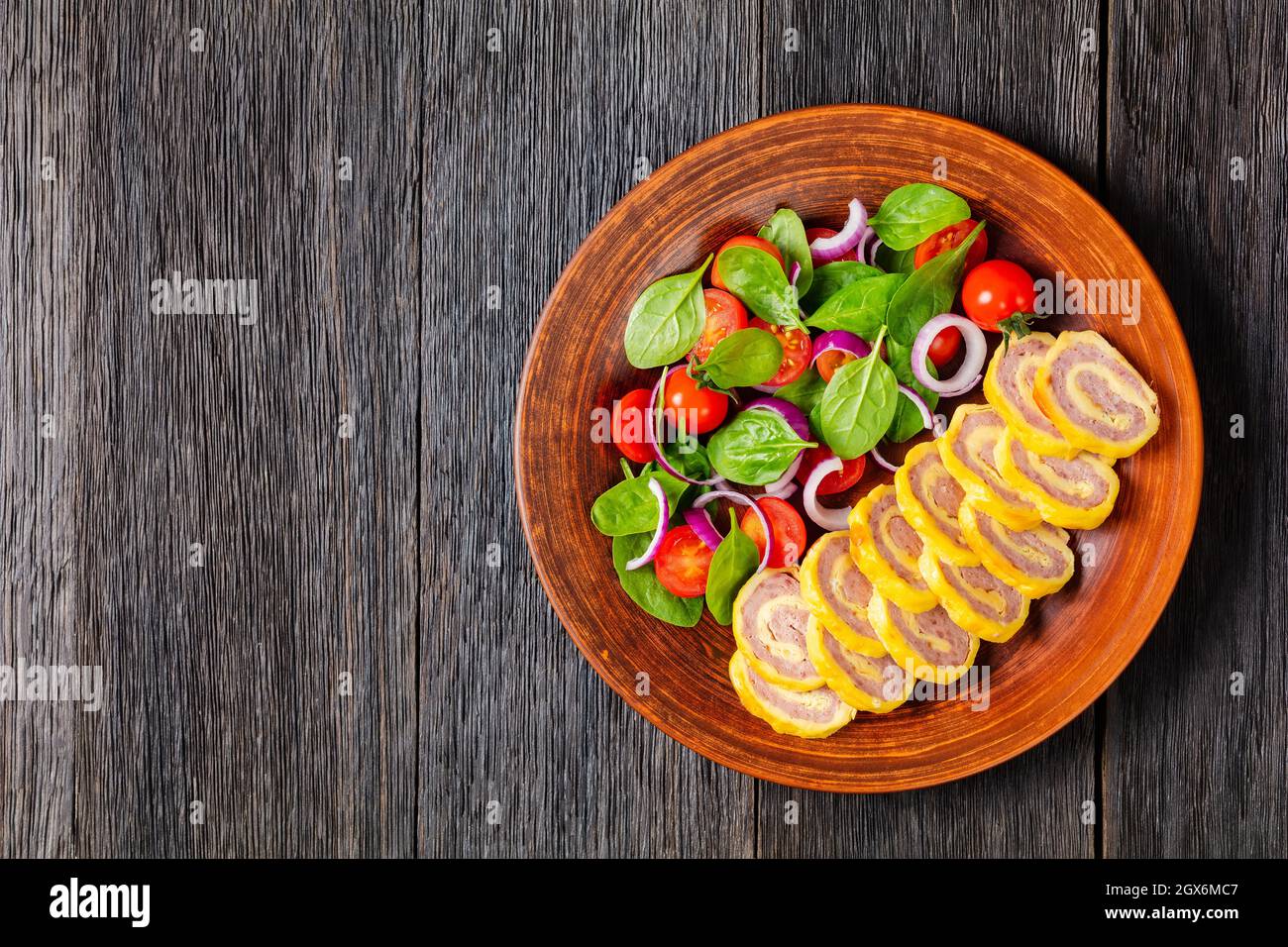 petit déjeuner au jambon et au fromage hachés petits roulés avec salade d'oignons rouges aux épinards frais sur une assiette rustique sur une table en bois, vue horizontale de Banque D'Images