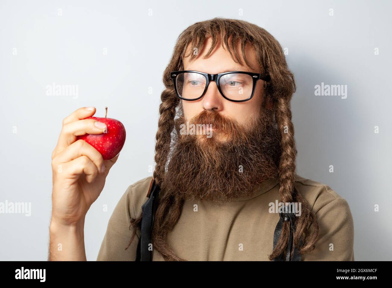 Scientifique pensif avec des tresses tenant la pomme à la main, regardant loin avec une expression réfléchie, homme à barbe chauve portant un T-shirt et des lunettes. Prise de vue en studio isolée sur fond gris. Banque D'Images