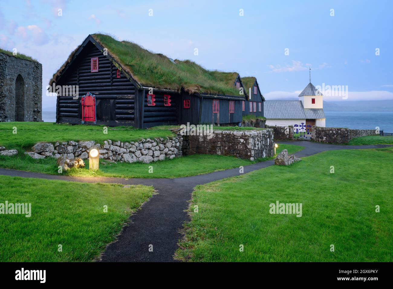 Ancienne ferme en rondins de Kirkjuboargardur avec toit en gazon et église d'Olavskirkjan dans le village de Kirkjubour sur Streymoy, îles Féroé Banque D'Images
