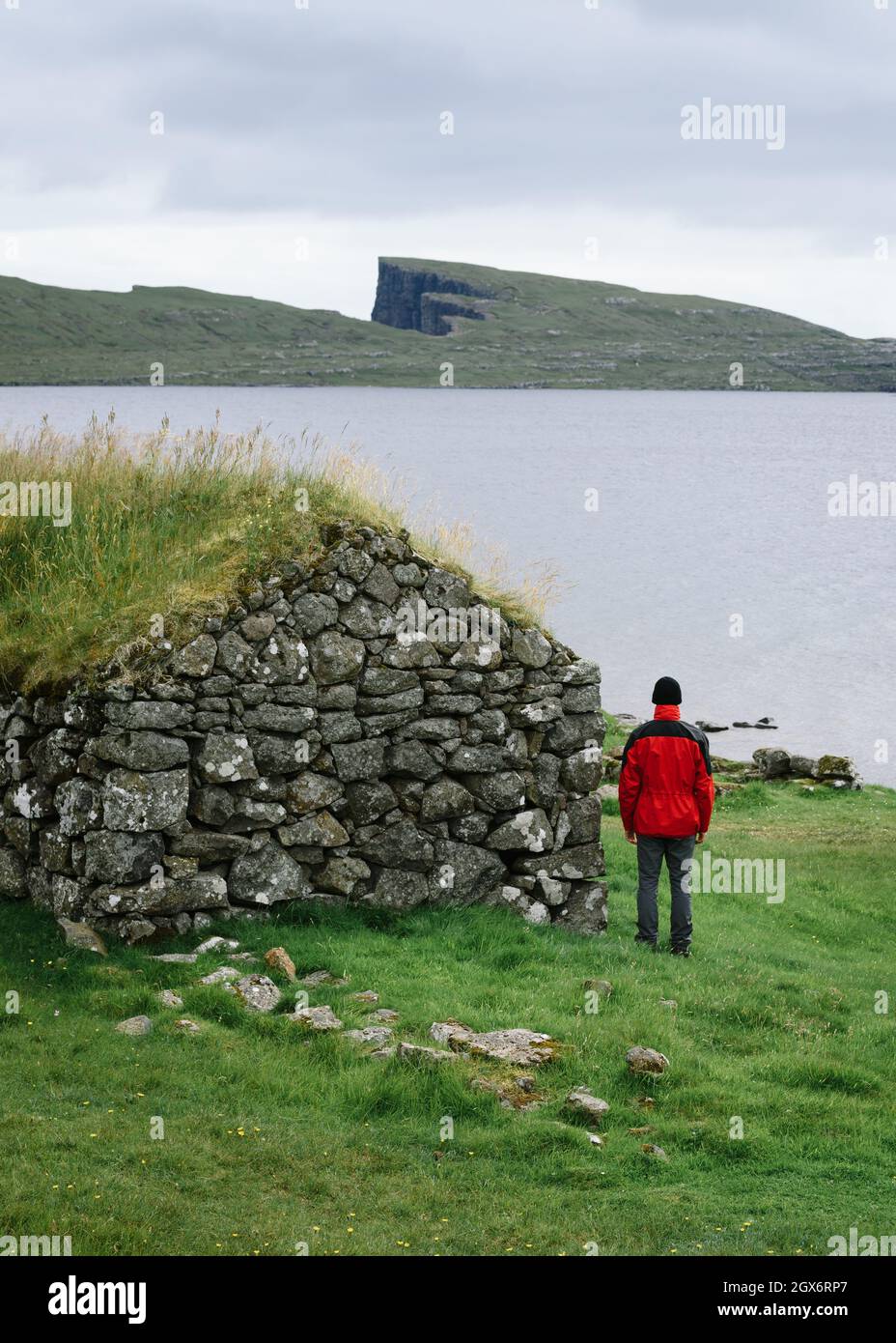 Un homme solitaire se tient près de maisons au toit de gazon près du lac Sorvagsvatn ou Leitisvatn sur les îles Féroé Banque D'Images