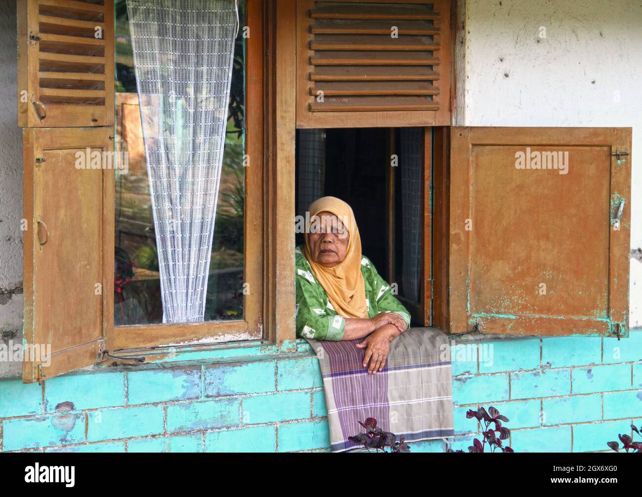 Une femme musulmane âgée portant un hijab vert regardant par sa fenêtre près de la ville de Bukittinggi sur Sumatra Ouest, Indonésie. Banque D'Images