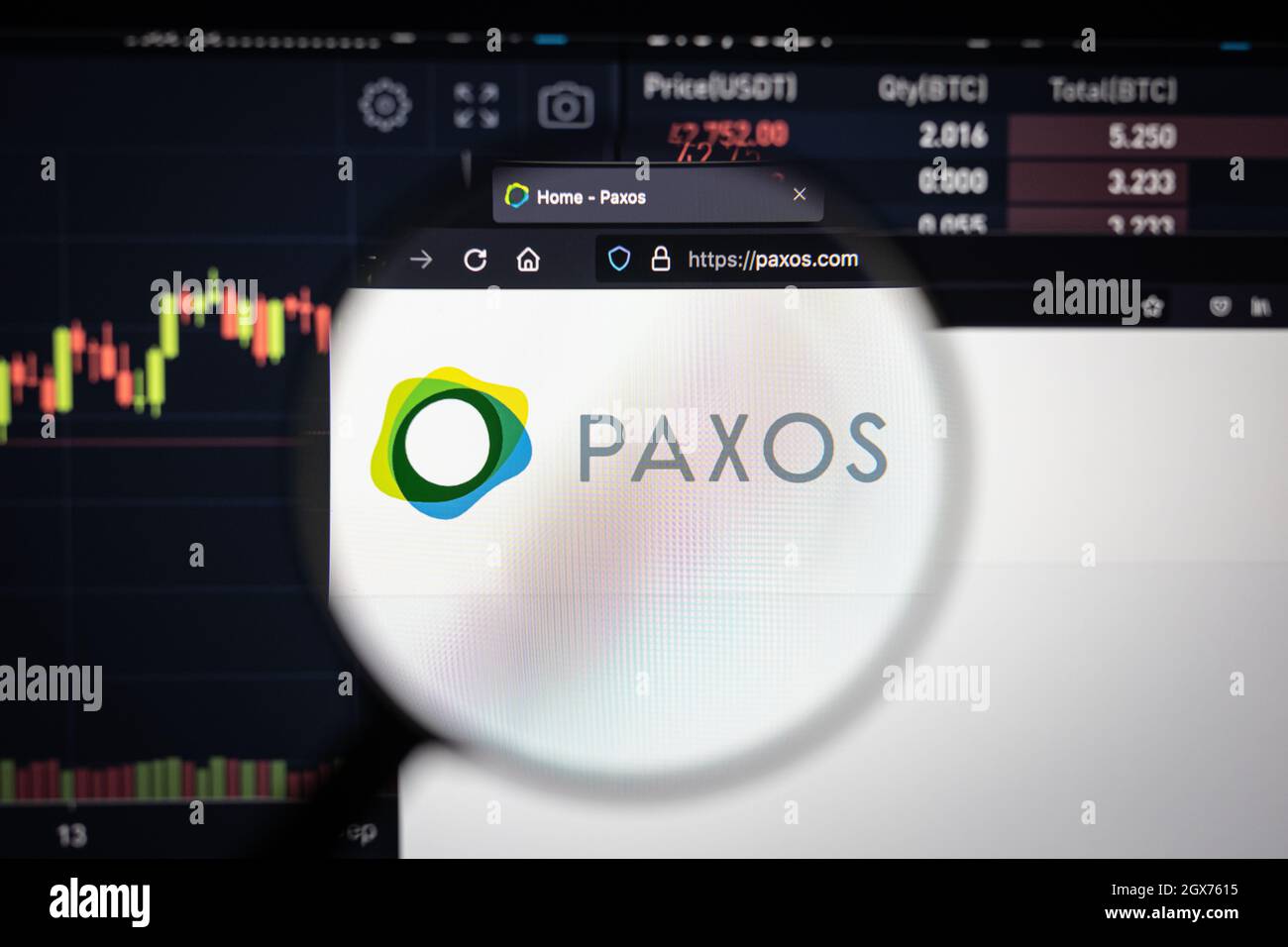 Le logo de la société Paxos sur un site Web avec des développements flous de marché boursier en arrière-plan, vu sur un écran d'ordinateur à travers une loupe Banque D'Images