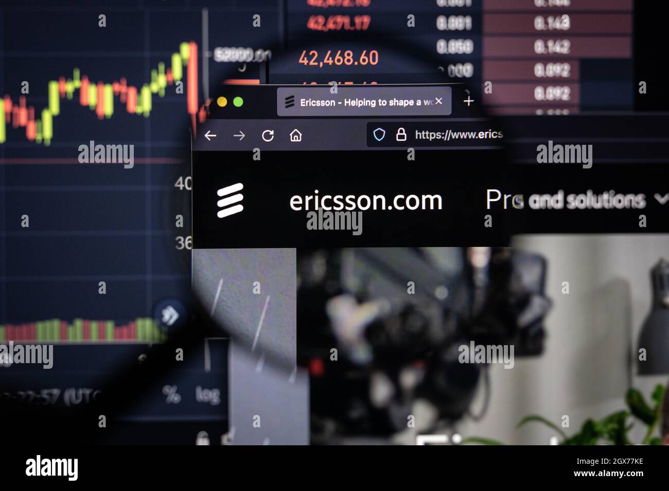 Ericsson.com logo de la société sur un site web avec des développements flous de marché boursier en arrière-plan, vu sur un écran d'ordinateur à travers une loupe Banque D'Images