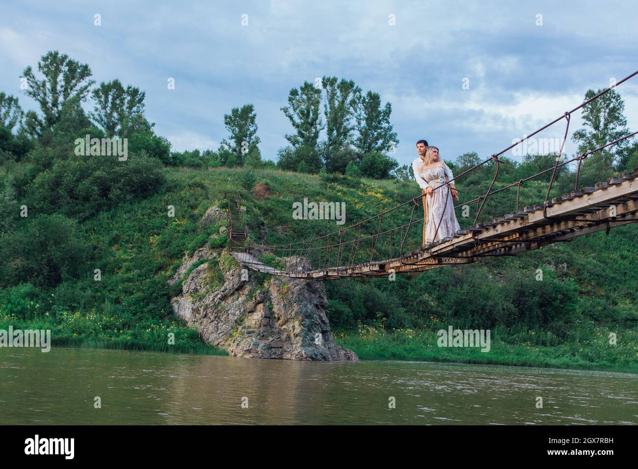 Beau jeune couple romantique debout et embrassant sur le pont suspendu au-dessus de la rivière Banque D'Images