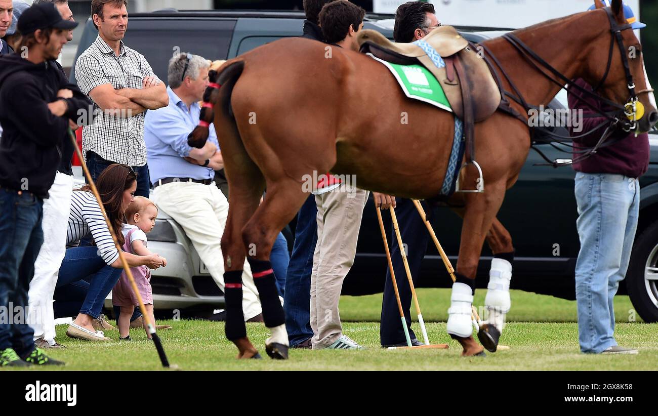 Le Prince George, tenu par sa mère Catherine, duchesse de Cambridge, est très tendre vers un cheval tandis que son père, le prince William, duc de Cambridge et oncle, le prince Harry, jouent dans un match de polo de charité au Cirencester Park Polo Club le 15 juin 2014. Banque D'Images