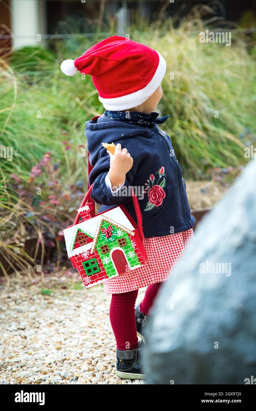 Petite fille habillée pour les promenades de Noël dans un parc avec sac de nouvel an.Chapeau rouge. Robe et collants, manteau bleu, sac en feutre en forme de maison d'hiver.Pas de face Banque D'Images