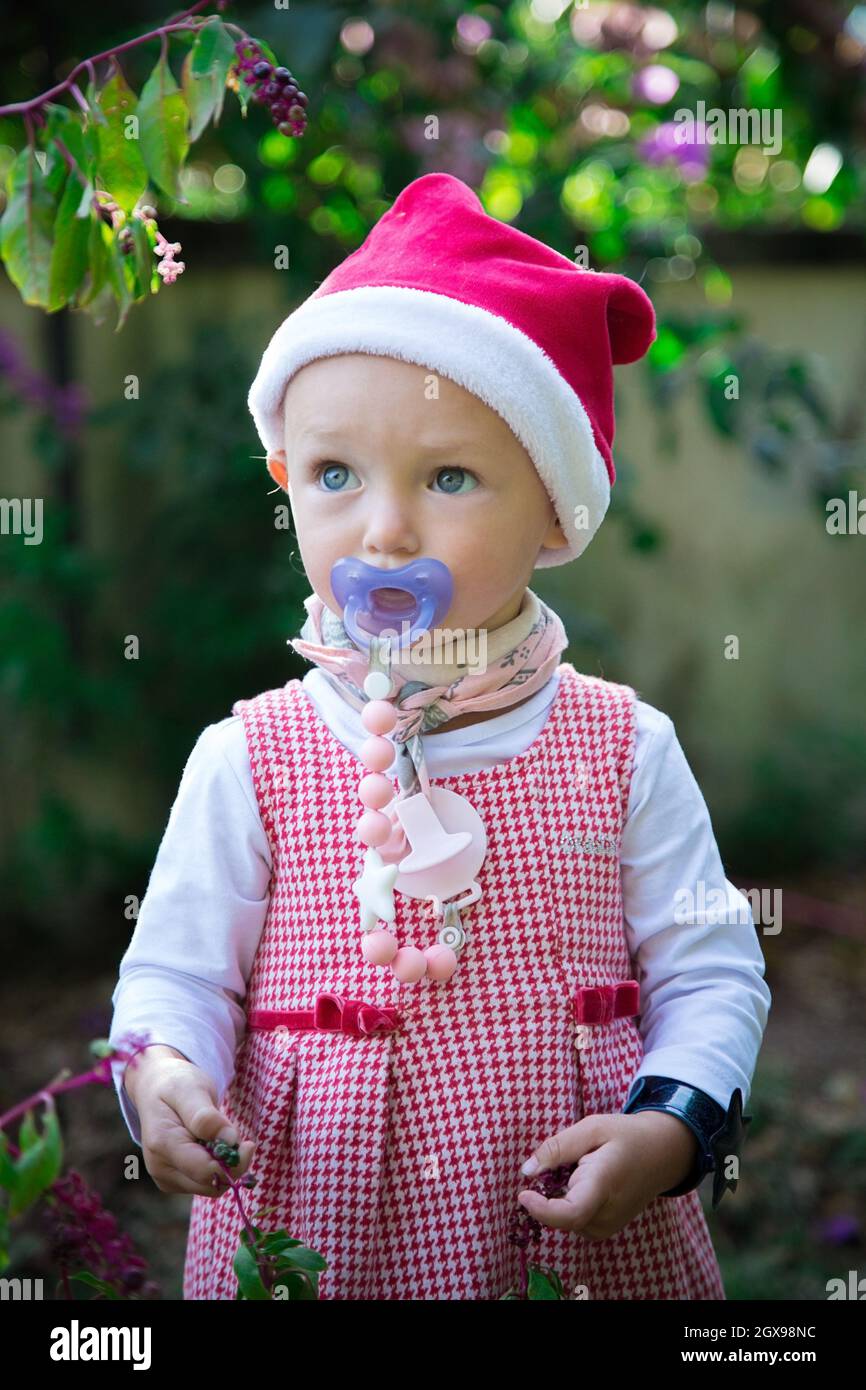 Petite fille oeil bleu en robe rouge et portrait de chapeau de Noël.Enfant avec sucette bleue en costume du nouvel an.Bébé mignon prêt pour l'hiver Banque D'Images