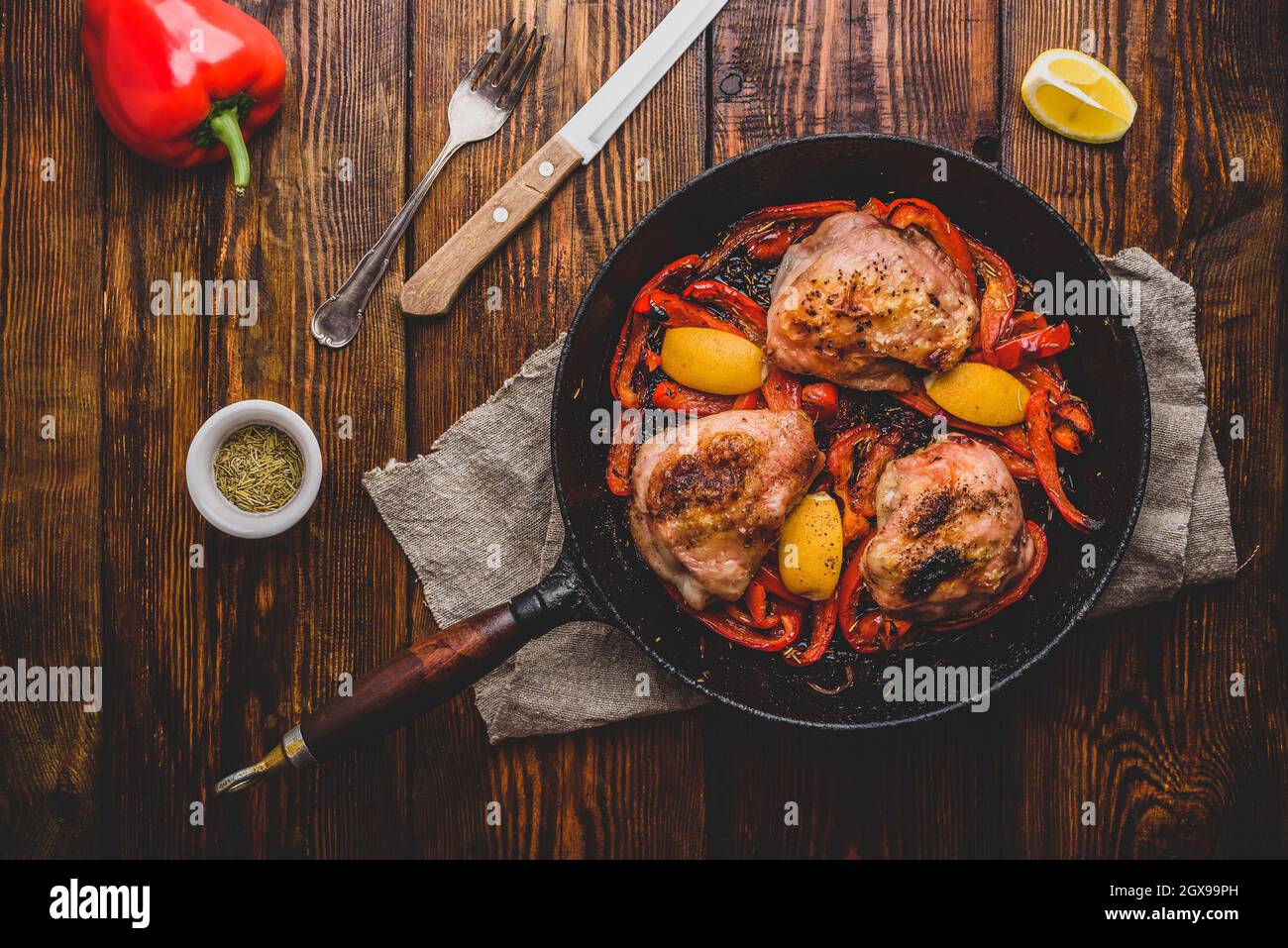 Cuisses de poulet cuites avec des poivrons rouges, du romarin et du citron dans une poêle en fonte. Vue de dessus Banque D'Images
