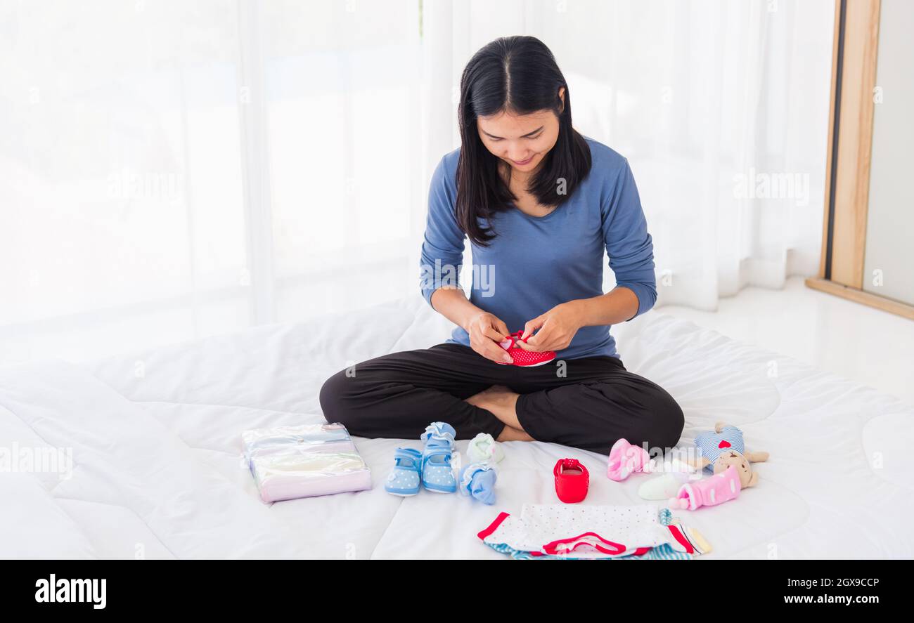 Mère asiatique préparant des vêtements de bébé se reposer et se détendre sur le lit elle fait l'achat de nouveaux vêtements de bébé pour après bébé se préparer à la naissance du nouveau-né Banque D'Images