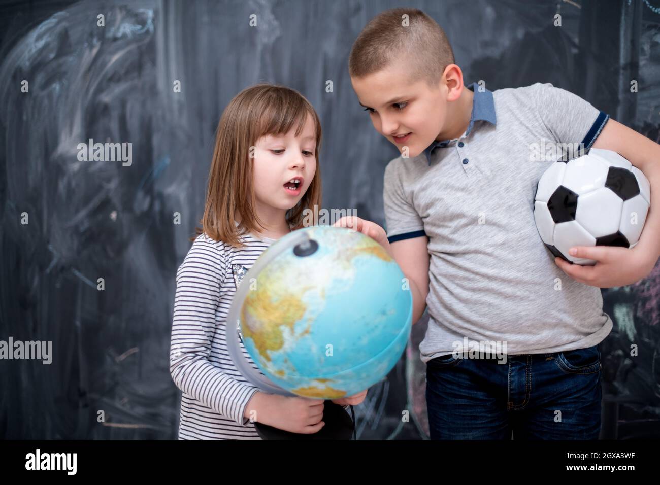 Enfants heureux garçon avec ballon de soccer et de petite fille sur le monde d'apprentissage à l'aide du globe terre alors qu'il se tenait devant le tableau noir Banque D'Images