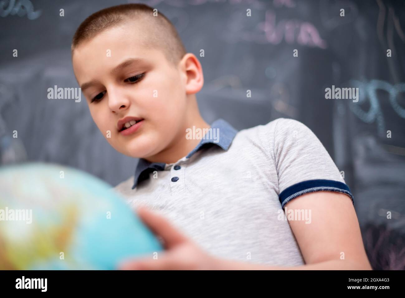 Happy cute boy apprentissage du monde en utilisant globe de terre alors qu'il se tenait devant le tableau noir Banque D'Images