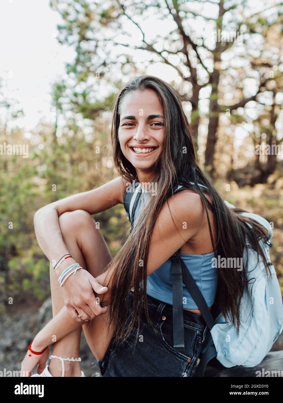 Femme adolescente souriante dans une gumshoe et un sac à dos tendance touchant l'avant-bras tout en regardant l'appareil photo sur la clôture à Tenerife Espagne Banque D'Images