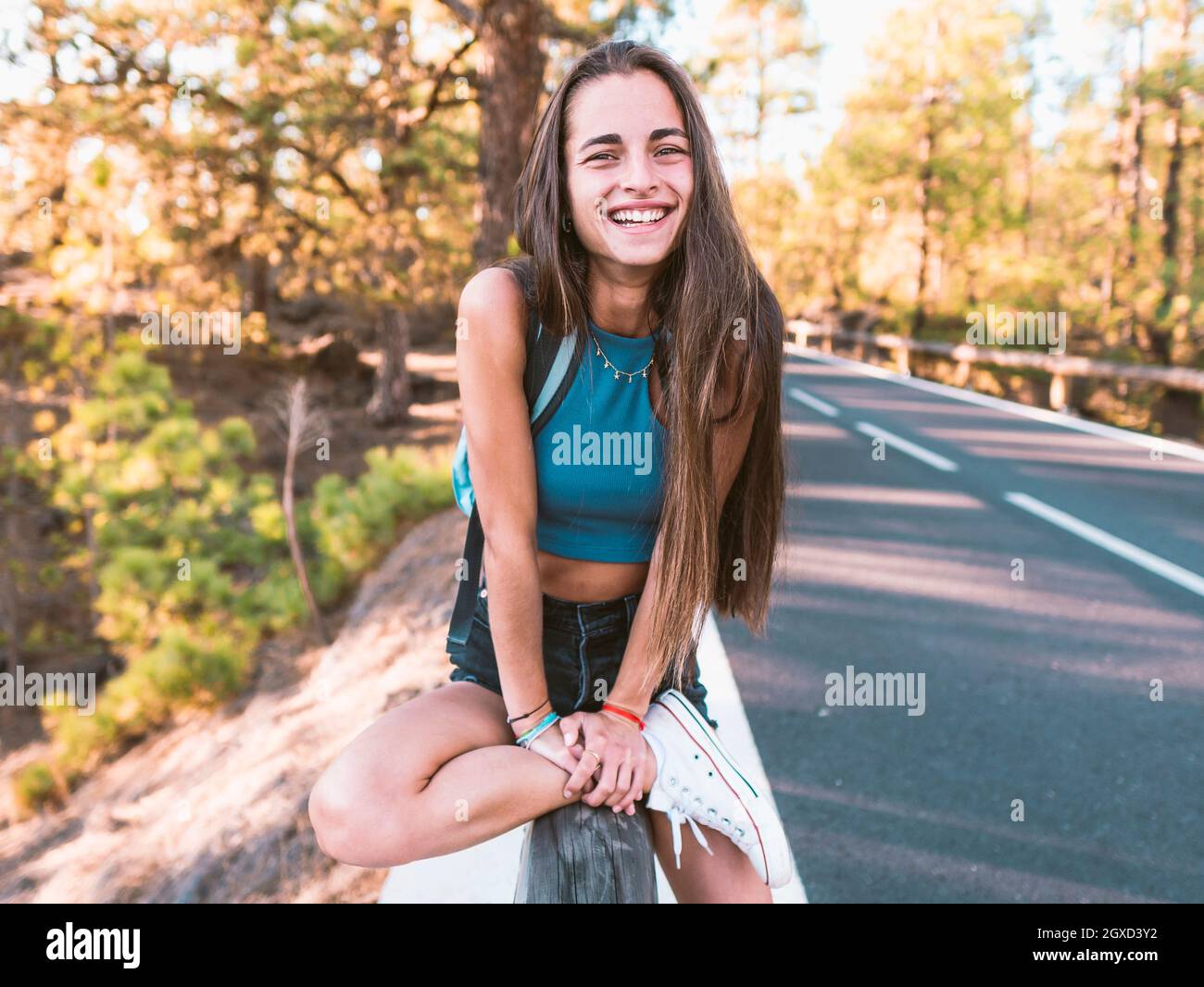 Femme adolescente souriante dans une gumshoe tendance touchant l'avant-bras tout en regardant la caméra sur la clôture à Tenerife Espagne Banque D'Images