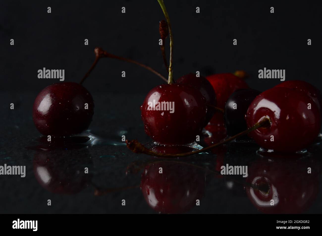 Cerises, avec des gouttes d'eau sur un fond noir avec réflexion Banque D'Images