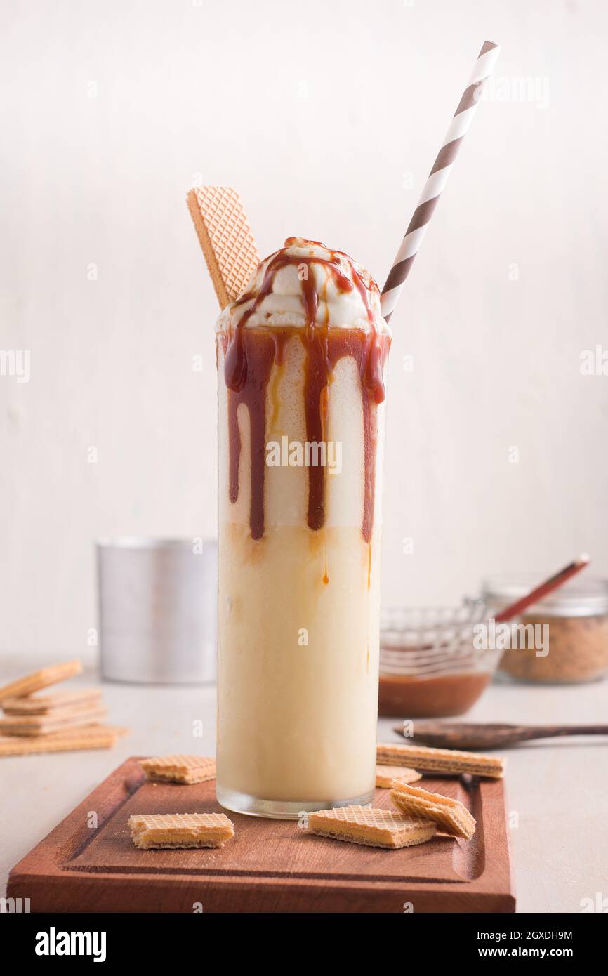 Verre avec milkshake au caramel sucré, glace à la vanille et biscuits cachets servis sur table Banque D'Images