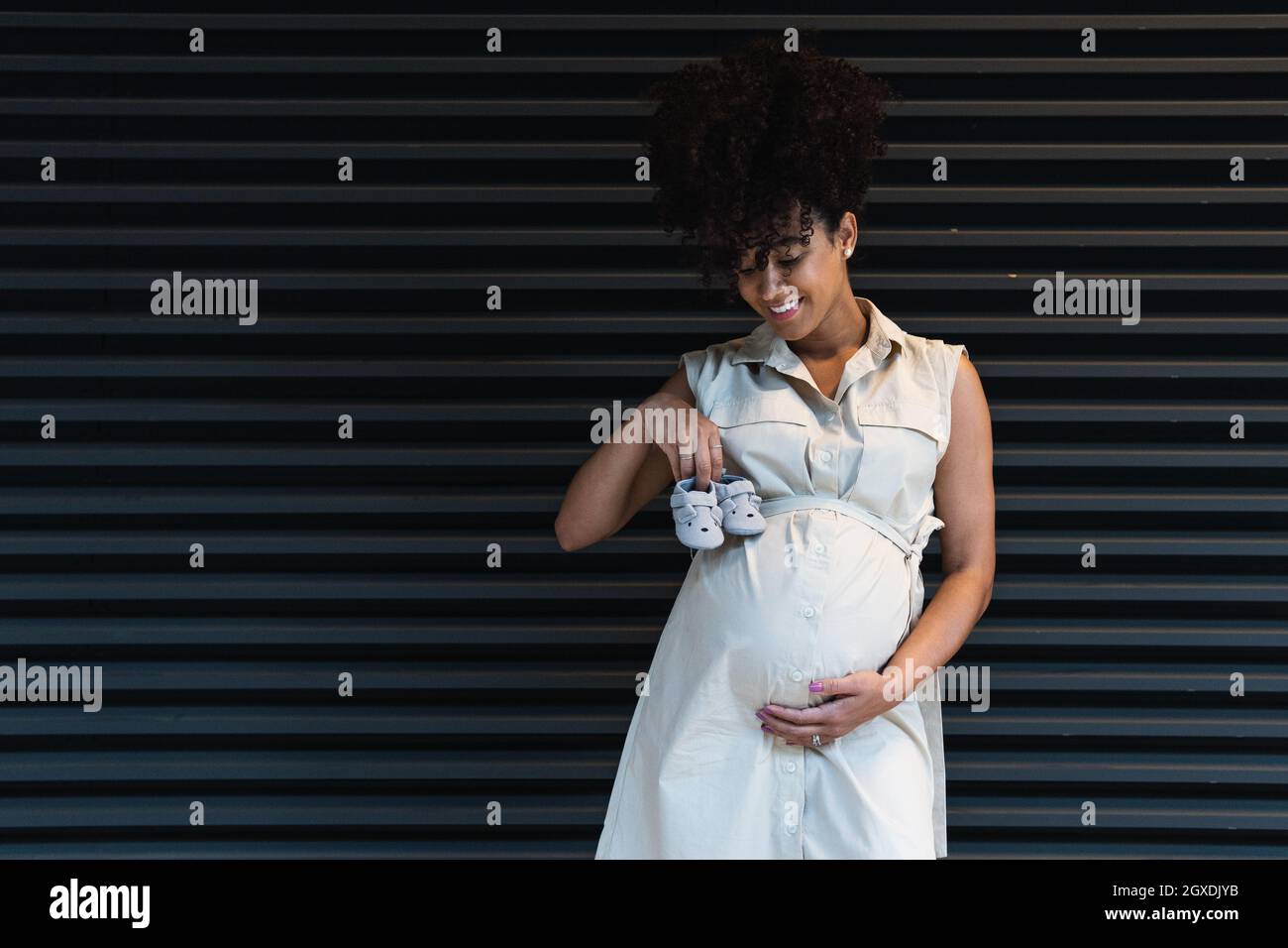 Une femme afro-américaine positive avec des cheveux bouclés anticipant l'accouchement montrant des chaussons de bébé et regardant vers le bas Banque D'Images