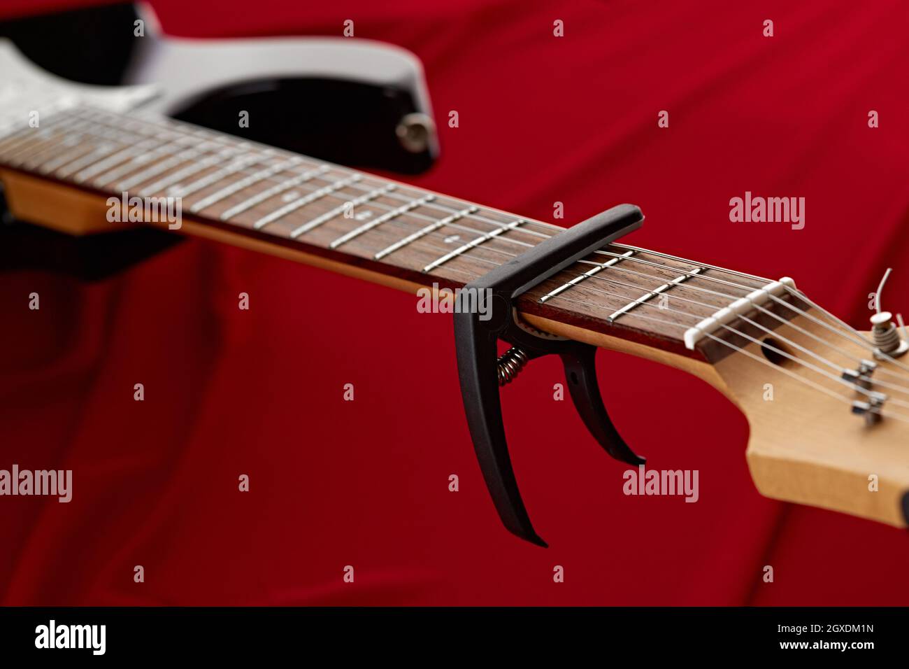Guitare électrique fretboard avec capodoster, gros plan, fond rouge, personne. Instrument de musique à cordes, son électro, musique électronique, équipement pour Banque D'Images