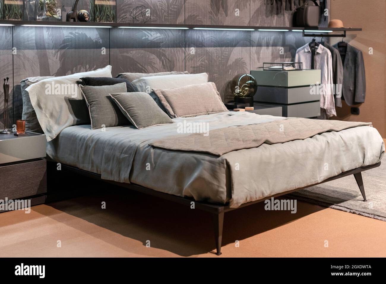 Décor intérieur d'une chambre de luxe monochrome minimaliste avec lit double de style divan, costumes suspendus sur un rack et frondes de palmiers tropicaux visibl Banque D'Images